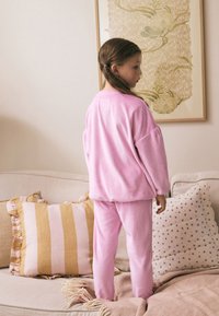 Ensemble de vêtements d'intérieur en polaire rose comprenant un pull ample et un pantalon assorti. Texture douce, avec des détails côtelés et une silhouette décontractée.