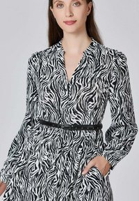 Robe à motifs zèbre avec des manches longues, un décolleté en V et une ceinture noire ajustée. Fabriquée en matériau léger avec une silhouette fluide.