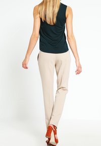 Top sin mangas verde oscuro, pantalones beige ajustados y zapatos de tacón naranja. Materiales suaves con una silueta ajustada y acentos mínimos.