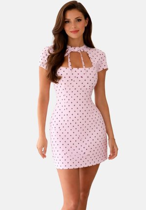 Femme aux longs cheveux bruns portant une courte robe rose à pois marron avec un décolleté en forme de trou clé noué au cou.