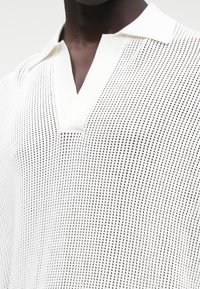 Biała, krótka koszulka polo z dzianiny z dekoltem w kształcie litery V, z teksturowanym, perforowanym wzorem i miękkim, gładkim kołnierzem.