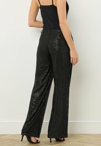 Zwarte paillettenbroek met een wijde pijp, voorzien van verticale strepen van pailletten voor textuur en glans. De tailleband is elastisch.