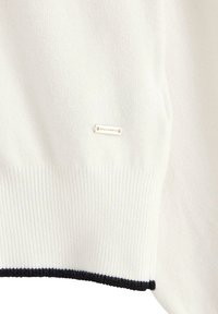 Pull blanc en maille avec une bordure côtelée aux ourlets et aux poignets. Comprend une petite étiquette de marque cousue sur le tissu. Accents de couleur foncée aux bords.