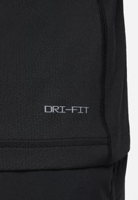Prenda deportiva negra DRI-FIT que muestra una tela texturizada con propiedades de absorción de humedad. Presenta detalles de costura a lo largo de las costuras.