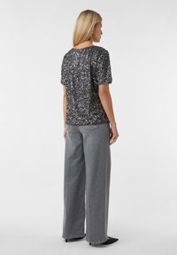 Schwarzes, mit Pailletten besetztes Kurzarm-Top kombiniert mit hellgrauen, weit geschnittenen Jeans und schwarzen spitzen High Heels, von hinten betrachtet.