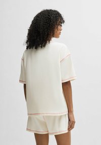 Krämfärgad bomullstop med korta ärmar, med kontrasterande rosa sömmar och en avslappnad passform, matchad med shorts i samma färg.