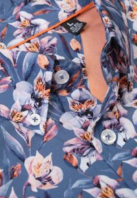 Bloemig shirt met een marineblauwe achtergrond en paarse en oranje bloemenpatronen, witte knopen en een contrasterende perzikkleurige binnenkraag.