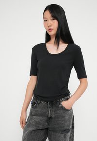 Camiseta negra de canalé con escote redondeado y mangas cortas, combinada con jeans de mezclilla oscuros con un ligero desgaste y detalles en los bolsillos.