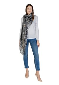 Giovane donna che indossa un top bianco a maniche lunghe, jeans skinny blu, tacchi alti beige e una grande sciarpa grigia con stampa leopardata e dettagli a catena.