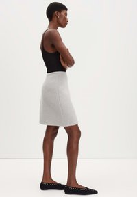 Grijze wollen rok met een lichte A-lijnvorm. Gecombineerd met een zwarte, fitted tanktop en zwarte flats met zilveren studs.