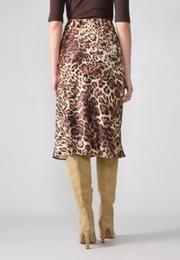 Satin midi suknja s uzorkom leoparda, s lepršavim rubom, u kombinaciji s bež čizmicama do koljena od brušene kože.
