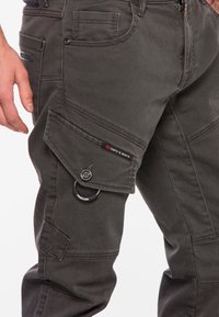 Donkergrijze cargobroek van een gestructureerde stof, met meerdere zakken, een flapzak aan de zijkant en een metalen ringaccent.