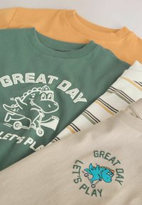 Drei Hemden: ein grünes Hemd mit einem Dinosauriermotiv, ein gestreiftes weiß-beiges Hemd und ein gelbes Hemd. Weiche Baumwolle, abgerundete Ausschnitte.