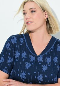 Top blu navy con scollatura a V realizzato in tessuto morbido, caratterizzato da una stampa floreale in azzurro chiaro con righe verticali e cuciture decorative lungo il collo.