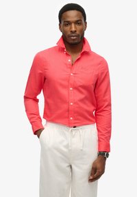 Camisa de botón coral de algodón con mangas largas, bolsillo en el pecho y botones blancos, combinada con pantalones cortos blancos con cordón.