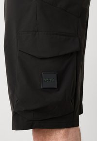 Pantaloni scurți negri tip cargo, dintr-un material texturat, cu un buzunar lateral cu clapetă și un patch pătrat cu logo-ul "BOSS" pe piciorul stâng.