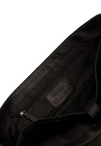 Indvendigt i en sort lædertaske med en lynlåslomme og et mærke med teksten "VENEZIA Genuine Leather" på en tekstureret stofbaggrund.