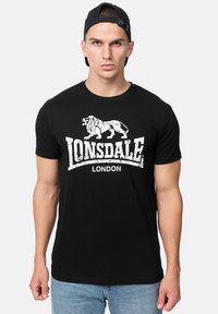 Sort bomulds T-shirt med et hvidt løvegrafik og teksten "Lonsdale London", klassisk rund halsudskæring, korte ærmer og tætsiddende design.