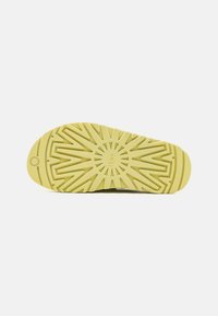 Semelle de chaussure en caoutchouc jaune clair, avec un motif texturé et géométrique ainsi qu'un logo. Le design assure une bonne adhérence et une durabilité.