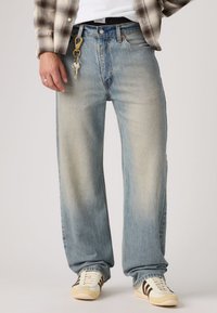 Ανοιχτό μπλε τζιν με ίσια γραμμή, κατασκευασμένο από τζιν υλικό, με ξεθωριασμένο φινίρισμα, σχέδιο με πέντε τσέπες και μπρελόκ προσαρτημένο στο θηλάκι της ζώνης.