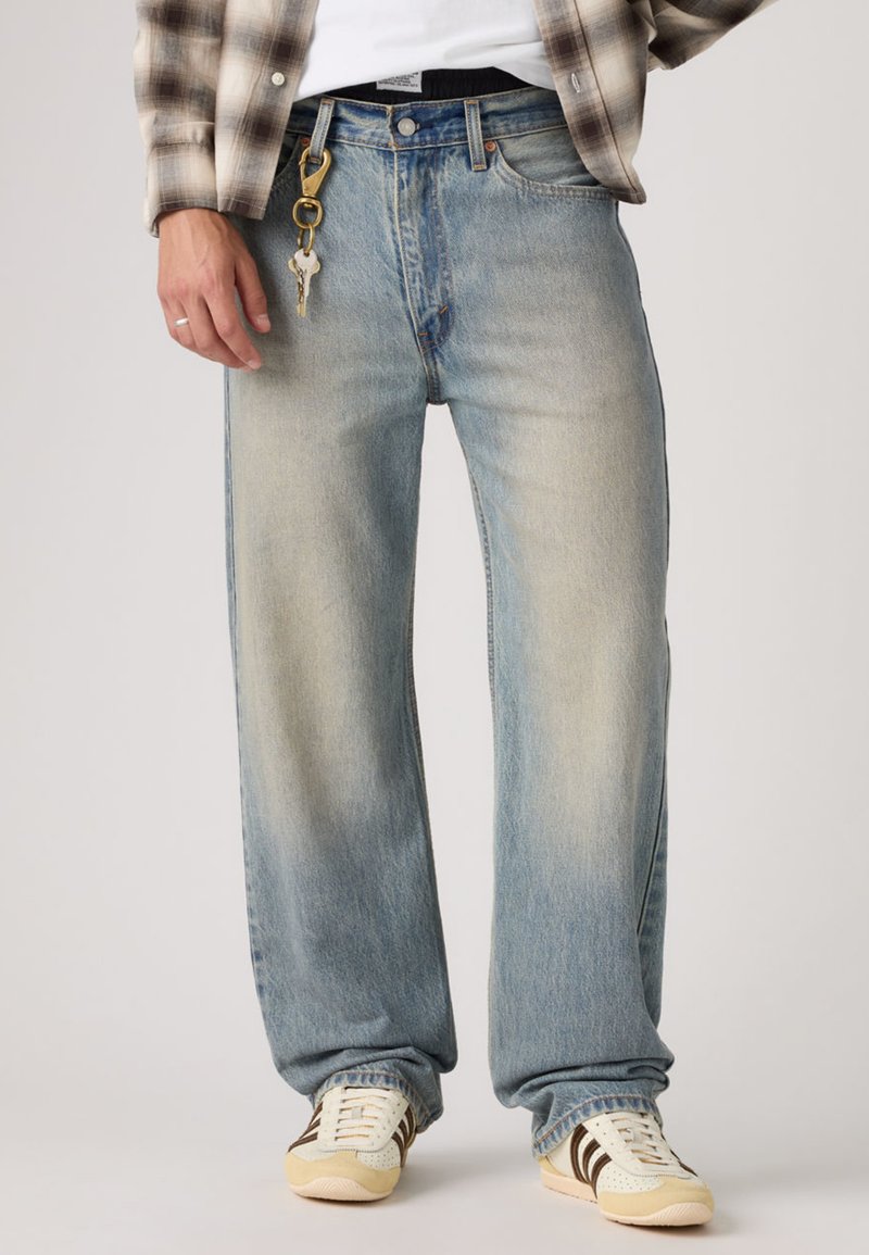 Ανοιχτό μπλε τζιν με ίσια γραμμή, κατασκευασμένο από τζιν υλικό, με ξεθωριασμένο φινίρισμα, σχέδιο με πέντε τσέπες και μπρελόκ προσαρτημένο στο θηλάκι της ζώνης.