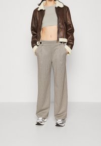 Brun läderbomberjacka med krämfärgad shearlingtrim, grå kort topp och breda beiga rutiga byxor. Silverfärgade sneakers fulländar outfiten.