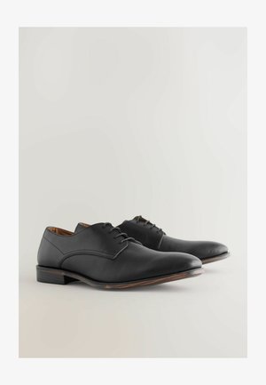 Zwarte leren dresschoenen met een gladde afwerking, ronde neus en een lage hak. Beschikt over een vetersluiting en gestikte accenten langs de randen.