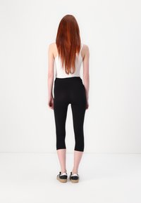 Svarte capri leggings laget av strekkbart stoff, med høy midje og en glatt tekstur, kombinert med svarte og hvite joggesko.