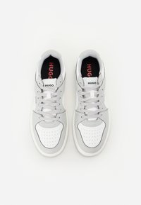 Sneaker bianche e grigie con una tomaia perforata, lacci grigi piatti, colletto imbottito e logo HUGO sulla linguetta e sul lato.