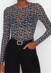Top trasparente a maniche lunghe con un motivo leopardato grigio e nero. Abbinato a jeans neri a vita alta e una cintura nera con fibbia dorata.