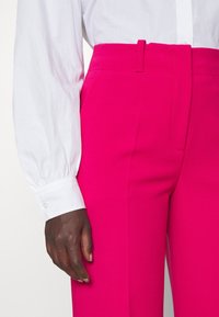 Fuchsia op maat gemaakte broeken met een hoge taille, met een soepele textuur en een voornaaddetail, gecombineerd met een witte blouse met knopen.