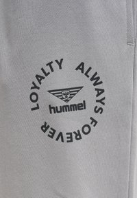 Graue Sweatpants aus weichem Stoff, mit einem runden schwarzen Druck, der den Text "LOYALTY ALWAYS FOREVER" und das "hummel"-Logo in der Mitte zeigt.