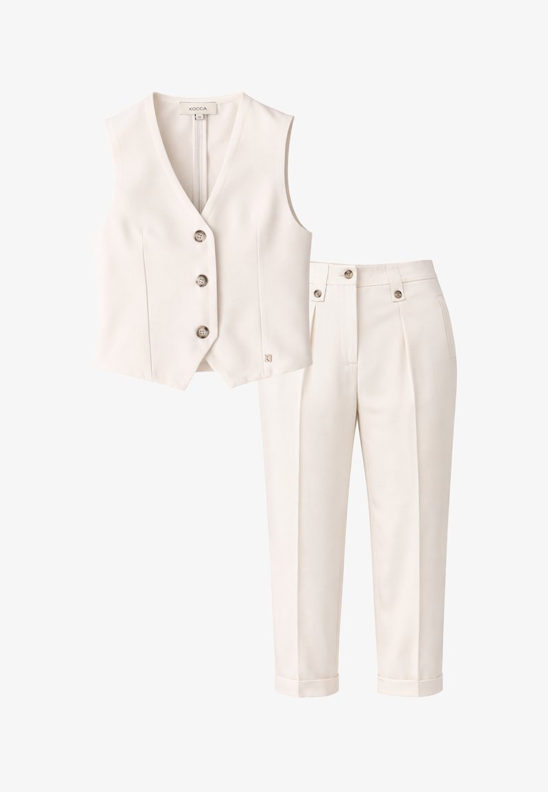 Gilet color crema sartoriale con tre bottoni abbinato a pantaloni abbinati a vita alta con risvolti e dettagli con bottoni.