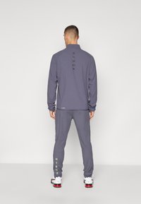 Langermige grijze sporttop met het 'HYROX' logo in het zwart op de achterkant, gecombineerd met bijpassende grijze sportbroek met groene 'HYROX' tekst.