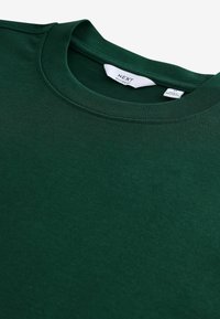 Dunkelgrünes Baumwoll-T-Shirt mit Rundhalsausschnitt, mit lockerer Passform. Etikett im Kragen sichtbar. Glatte Textur, keine Muster oder Akzente.