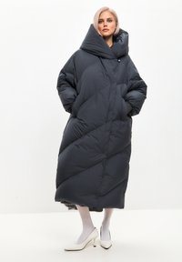 Padded, tamno sivi oversized kaput s visokim ovratnikom, dijagonalnim šavovima i bočnim džepovima. Nositi preko bijelih čarapa i potpetica.