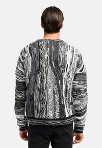 Sorte og hvide mønstrede strikkede sweater med et struktureret design, der indeholder forskellige geometriske former og uregelmæssige linjer. Ribbestrikkede manchetter og kant.