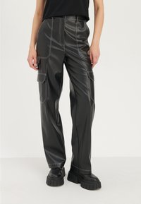 Pantalon cargo en simili cuir noir avec des coutures blanches, plusieurs poches, une coupe décontractée et des jambes larges, associé à des chaussures plates-formes noires chunky.