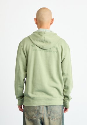 Groene hoodie gemaakt van zachte stof, met een voorzak in kangoeroestijl en bedrukte tekst op de achterkant, voorzien van ribgebreide boorden en zoom.