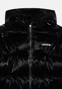 Svart pufferjacka med en glänsande yta, med dragkedja och huva. Vit Levi's-logotyp på bröstet. Mjuk innertextur.