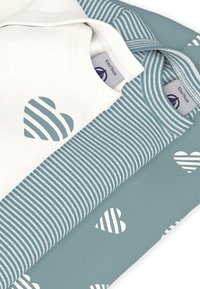 Τρία μπλουζάκια στοιβαγμένα το ένα πάνω στο άλλο: ένα ελεφαντόδοντο με καρδιά ριγέ, ένα πετρόλ ριγέ και ένα πετρόλ με λευκές καρδιές. Βαμβακερό ύφασμα, απαλή υφή.