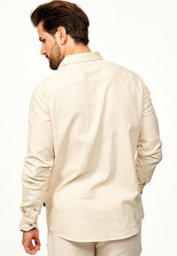 Helles beige Langarmhemd aus strukturiertem Stoff. Verfügt über einen spitzen Kragen, geknöpften Manschetten und einen abgerundeten Saum. Rückansicht gezeigt.