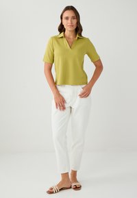 Limonengrünes, geripptes Polo-Shirt mit kurzen Ärmeln und V-Ausschnitt, kombiniert mit weißen, schmal zulaufenden Hosen und braunen, mehrschnürigen Sandalen. Minimalistisches Design.