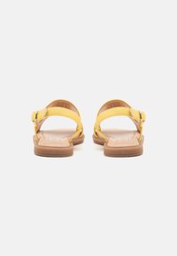 Sandalias de cuero amarillas con correas ajustables en el tobillo, suelas planas y un diseño simple. Textura suave, hardware minimalista y construcción ligera.