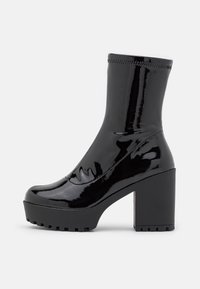 Botte de cheville en cuir verni noir avec un talon large et une semelle robuste, tige lisse avec des détails de coutures visibles.
