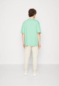 Camiseta de gran tamaño en verde menta con mangas cortas, combinada con joggers color crema. Confeccionada en material suave con un ajuste relajado. Diseño minimalista.