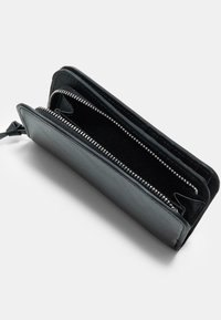 Crni kožni novčanik s zatvaračem na zip, koji ima dva odjeljka i glatku teksturu. Unutra je od mekog materijala s vidljivim šavovima.