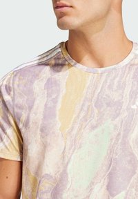 Kurzärmliges T-Shirt mit Rundhalsausschnitt im pastellfarbenen Wirbelmuster in Lila, Gelb und Grün. Verfügt über einen strukturierten Stoff und drei weiße Streifen an den Schultern.