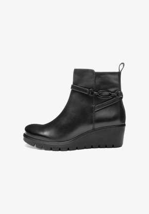Zwarte leren enkelboot met wiggenhak, decoratieve riem en kettingdetail, en een trekband aan de achterkant.