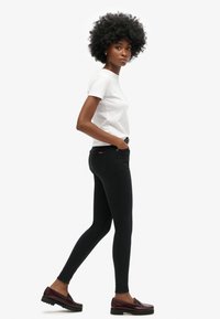 Zwarte skinny jeans met een hoge taille en een aansluitend ontwerp, gecombineerd met een wit T-shirt en bordeauxrode loafers, met een stijlvolle uitstraling.